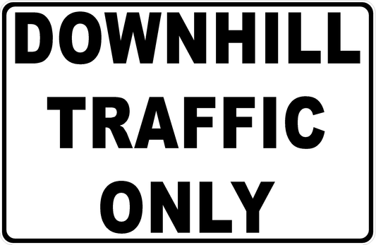 White rectangular sign with bold black “DOWNHILL TRAFFIC ONLY” lettering and a black border.